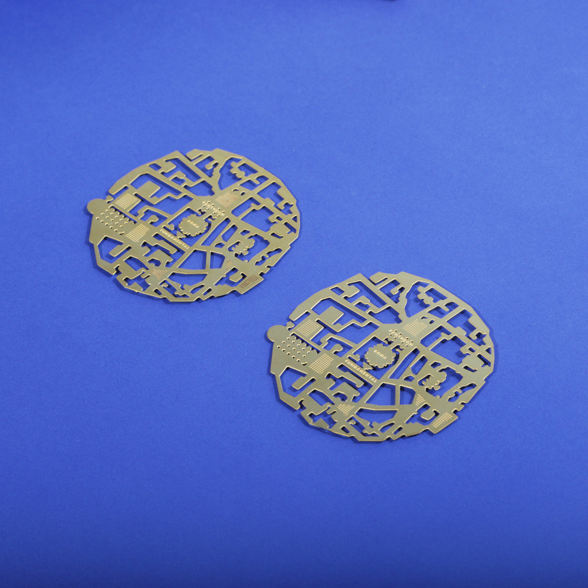 Two Roma brass coasters on a blue background