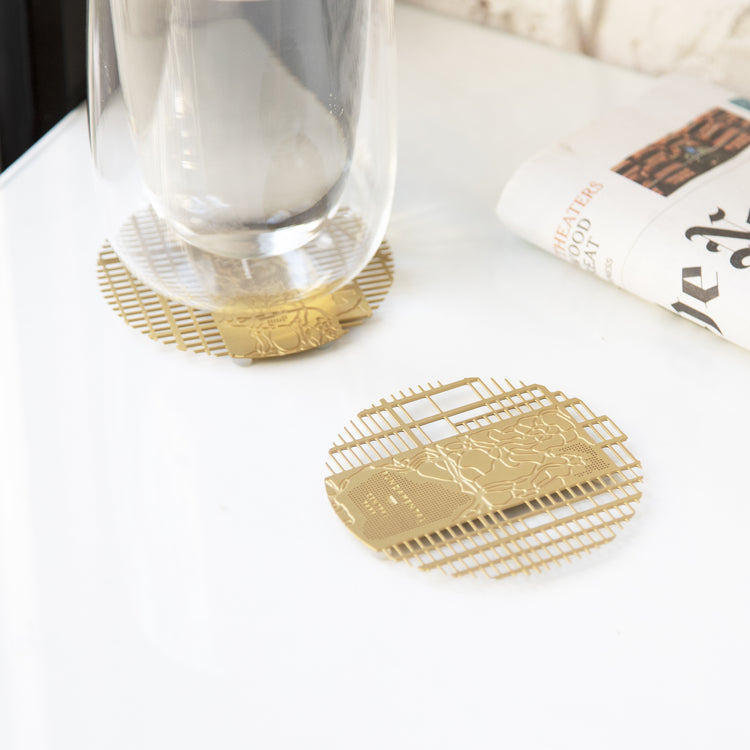 A Manhattan brass coaster under a glass beside an open book